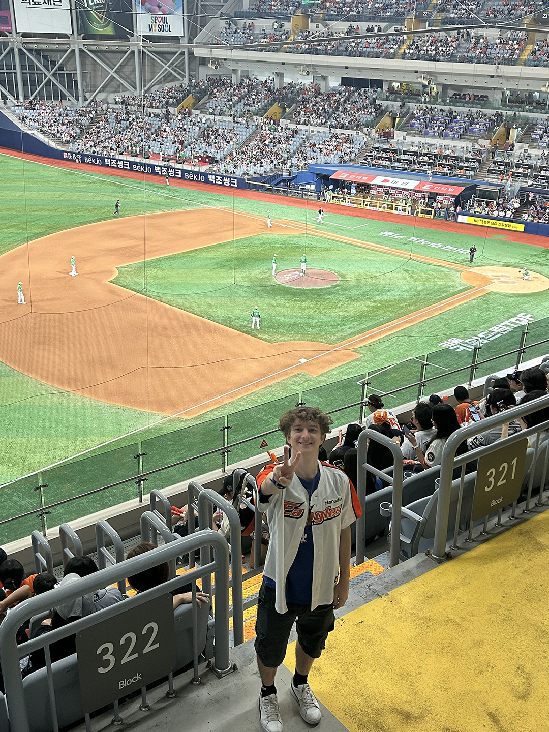 Camden standing in the stands at a baseball game with the infield behind him