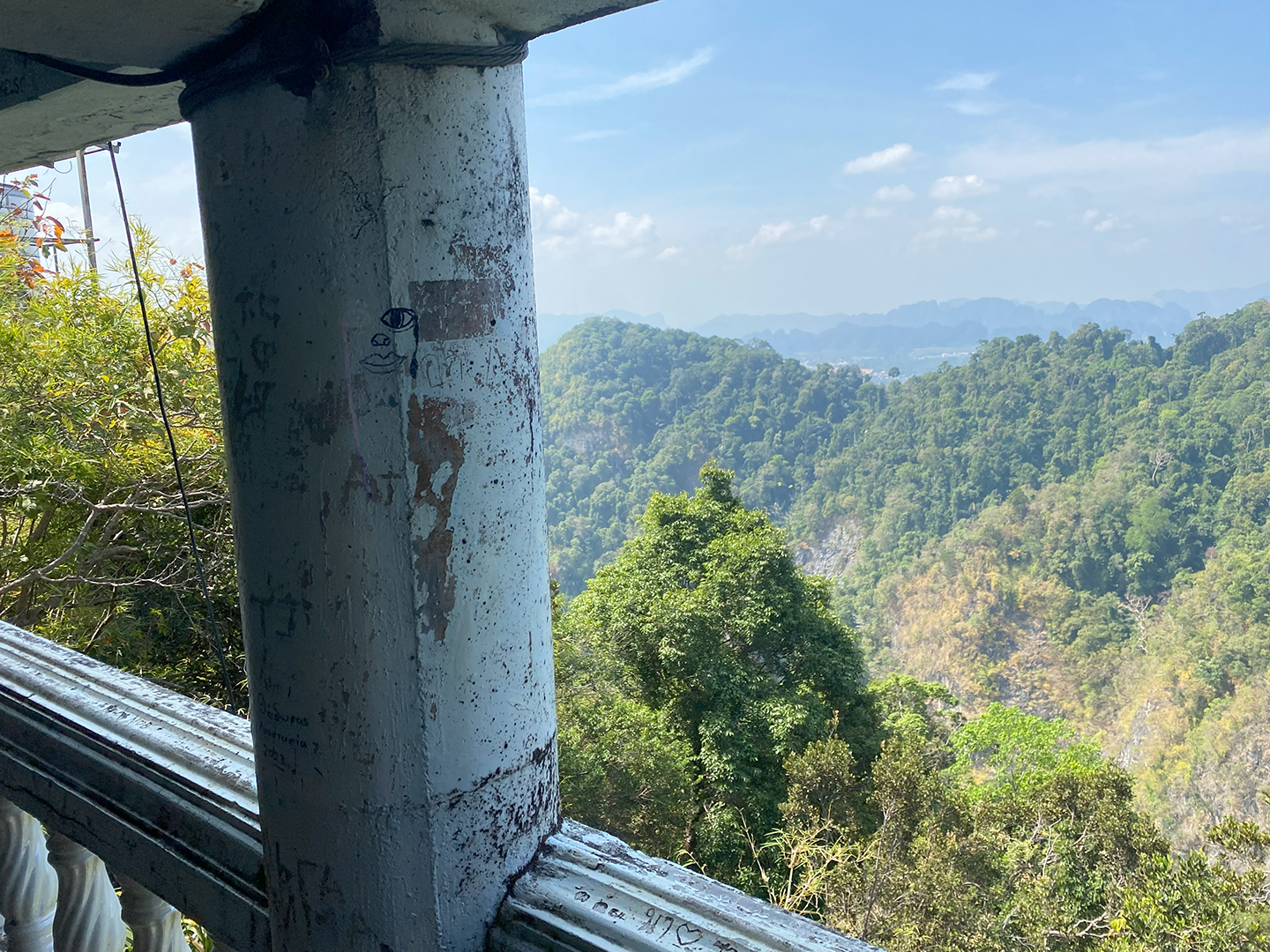 Looking out at the green, mountainous Thai landscape from the top of the mountain while standing under a stone structure